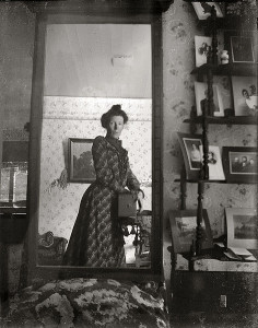 Black and white photo of a mirror showing a woman circa 1900 holding a camera